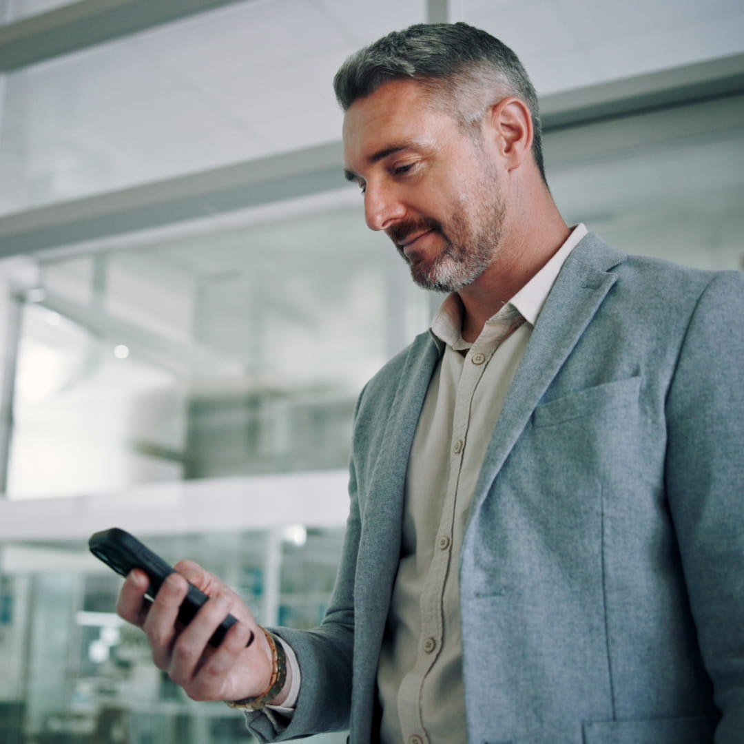 Man in gray suit smiling and looking at smartphone in modern office setting.
