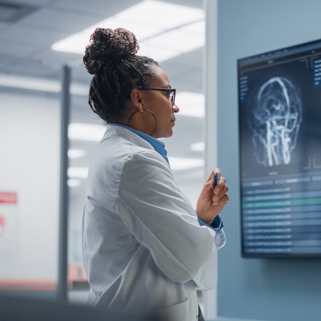 Doctor in a white coat examines a brain scan on a screen in a medical office.