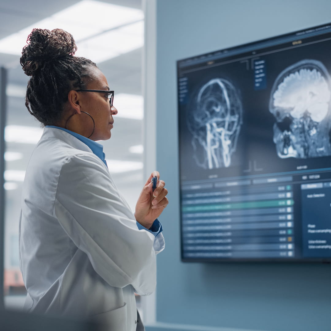 Doctor in a lab coat analyzing brain scans on a large screen in a modern medical facility.