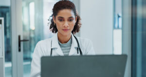 Happy woman, doctor and typing with laptop for medical study, news or telehealth at hospital. Female person or healthcare employee on computer for online medicine, research or communication at clinic.