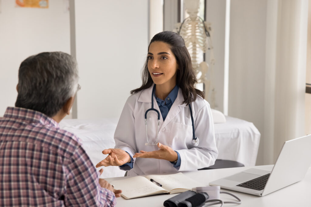 On medical appointment. Confident smart young female doctor family therapist sit at desk at hospital cabinet speak to elderly male patient explain diagnosis give recommendations on treatment therapy