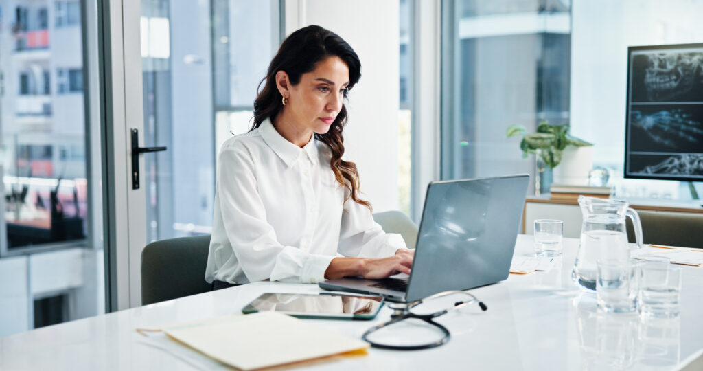Doctor, laptop and stethoscope with woman in hospital for cardiology, medical or telehealth. Computer, healthcare and typing report with professional in clinic for administration or management.
