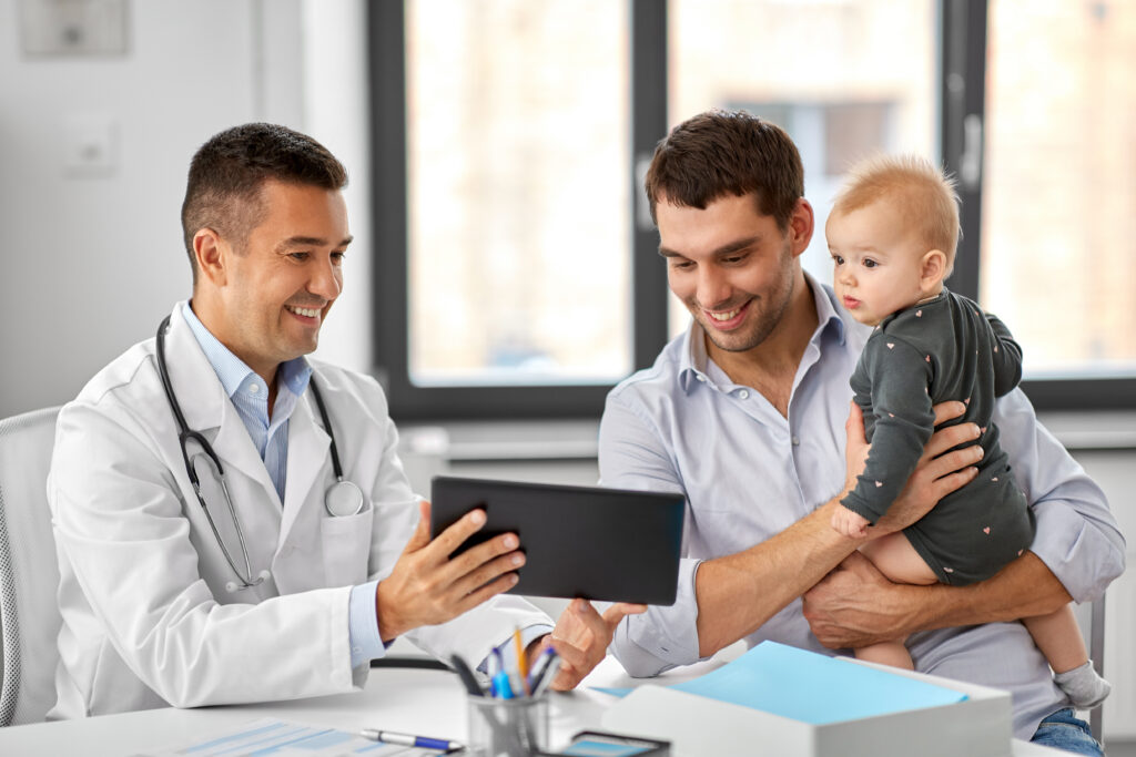 medicine, healthcare, pediatry and people concept - happy doctor showing tablet computer to father with baby daughter at medical office in hospital