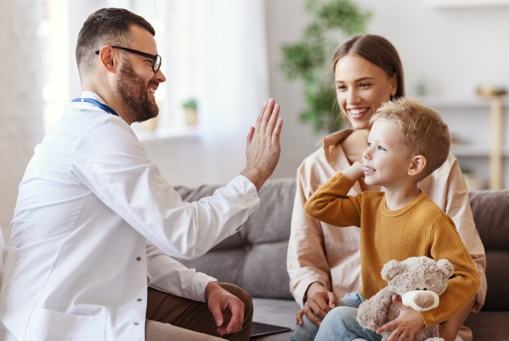 family doctor pediatrician conducts examination of child boy who came with his mother, and giving high five to him