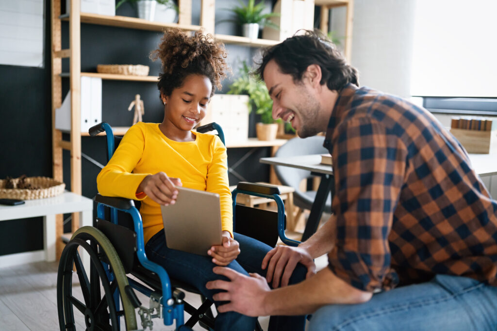 Multiethnic happy family activities. Child with disability in wheelchair at home having fun with father