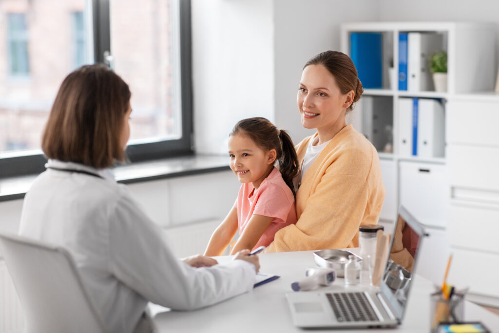 medicine, healthcare and pediatry concept - happy smiling mother with little daughter talking to doctor at clinic