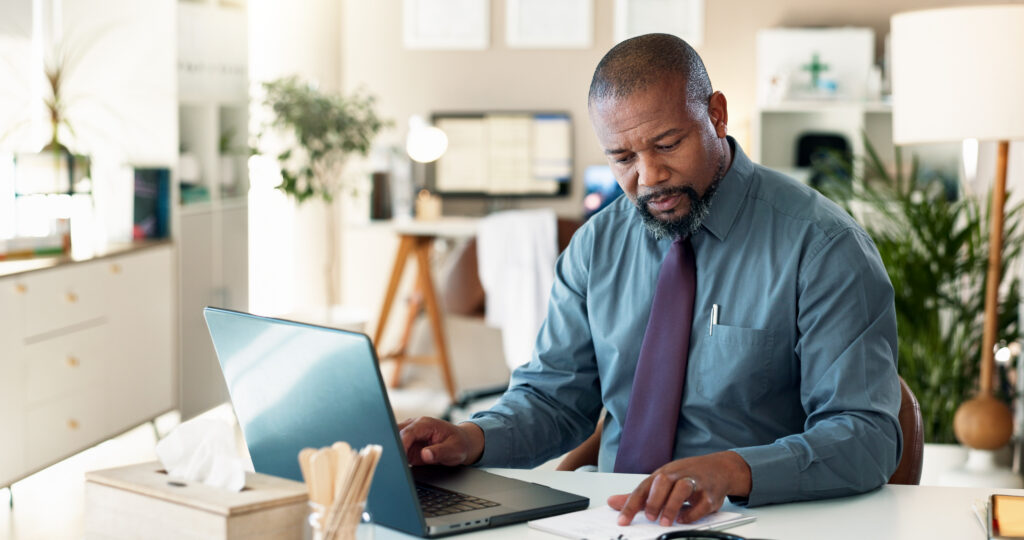 Reading, typing and man with laptop, healthcare and data entry with health records and information. Digital, documents and black person with app for research, patient navigator and online in hospital.