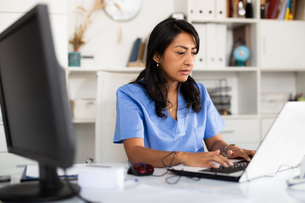 Focused Hispanic female doctor working with laptop in clinic office. Modern medicine and healthcare concept