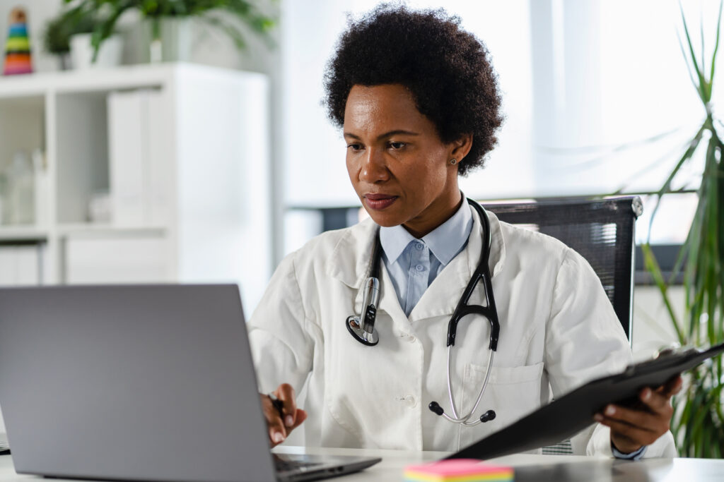 Reducing After-Hour Work With AI Clinical Documentation Female doctor working at her office in front of laptop computer, writing a health report