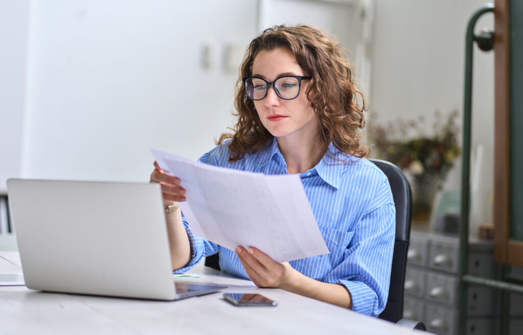 Why Revenue Cycle Intelligence Matters for Growing Practices Young busy business woman manager, lawyer or company employee holding accounting bookkeeping documents checking financial data or marketing report working in office with laptop. Paperwork management