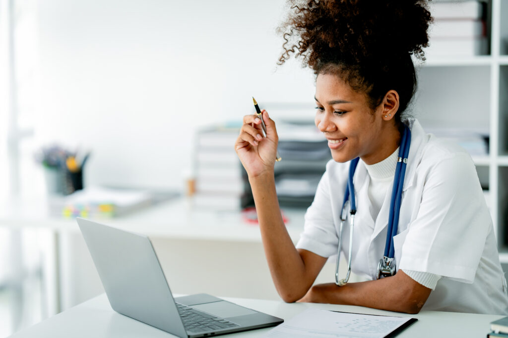 Why Revenue Cycle Intelligence Matters for Growing Practices African american female doctor working on laptop, filling out paperwork, patient medical history, reviewing documents at her workplace medical and health concept