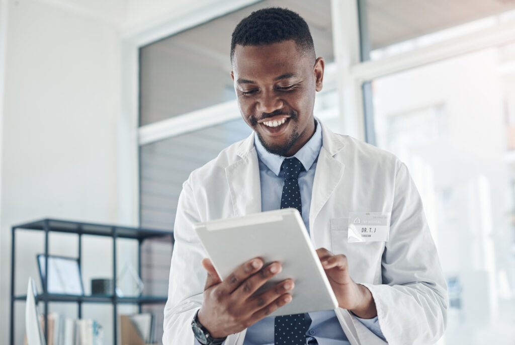 Reducing After-Hour Work With AI Clinical Documentation Doctor, black man and happy with tablet online results of electronic health records, improved patient wellness and reading. Medical worker, digital technology and proud for progress and telehealth