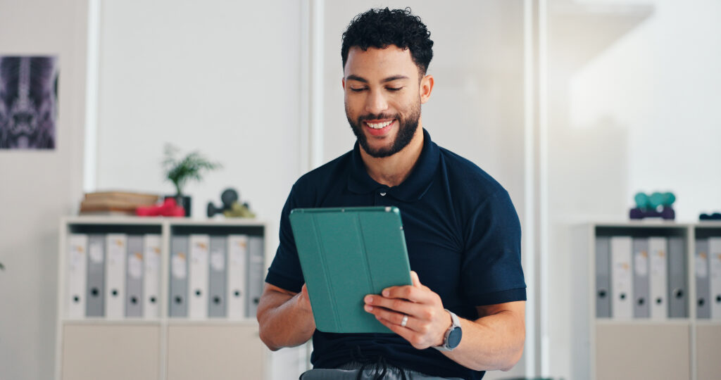 Man, physiotherapist and tablet in office with smile, registration and healthcare service. Chiropractor, happy and tech in private practice for reflexology, patient schedule and physiotherapy startup.
