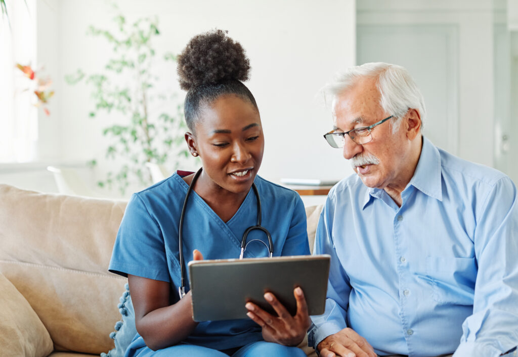 How to Know When It's Time to Switch EHR Systems Doctor or nurse caregiver showing a tablet screen to senior man and laughing at home or nursing home