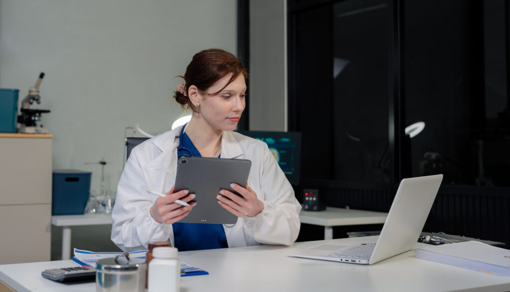 The Challenges Practices Face When Switching EHR Software Doctor working on laptop and tablet and medical on clipboard on desk, electronics medical record system EMRs concept.