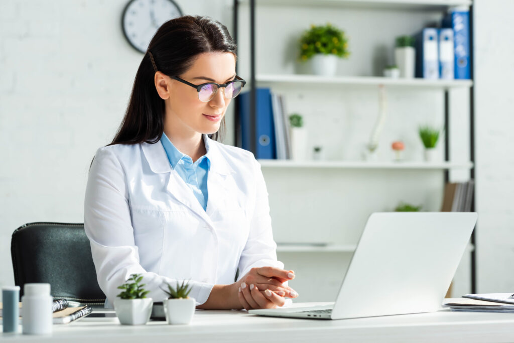 Improving Revenue Cycle Management Without Expanding Staff confident doctor having online consultation with patient on laptop in clinic office