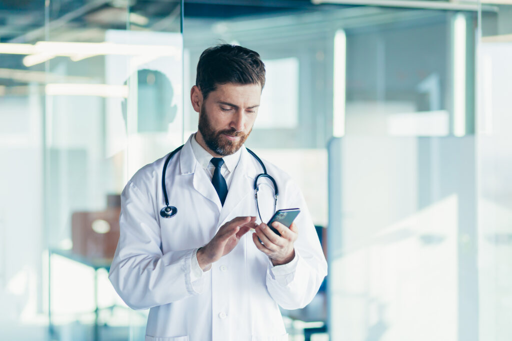 What Patients Expect From Modern Healthcare Apps Male doctor in a white coat in a modern clinic reads information from a mobile phone corresponds with colleagues happy and smiles