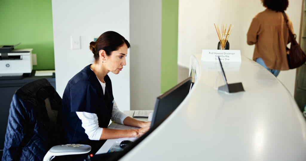 How Fax Automation Reduces Front-Office Administrative Work Clinic, receptionist and woman on computer for medical service, appointment and administration. Healthcare, hospital and dental assistant at front desk for planning, online schedule and information.
