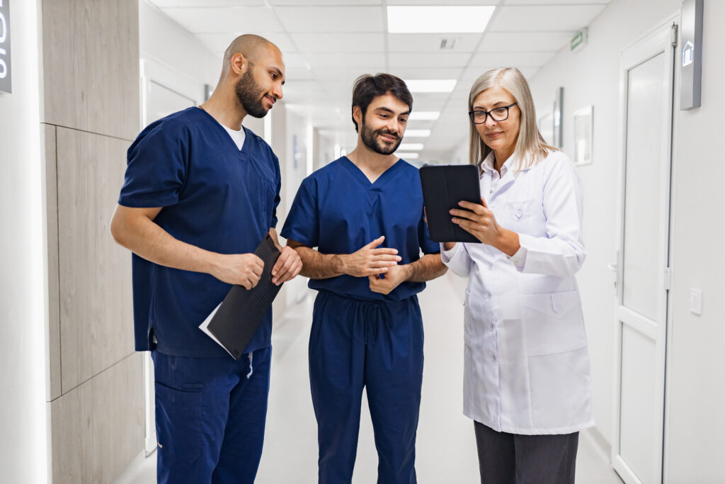 A doctor and two nurses review a tablet in a clinic hallway, discussing patient information and medical records.