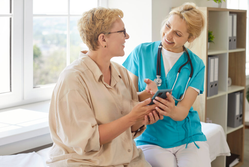 Streamlining the Transition to New Patient Portal Software Nurse showing health results to happy senior patient on smartphone during clinic visit, explaining how to use health mobile app easy. Smiling woman using mobile phone with help of doctor
