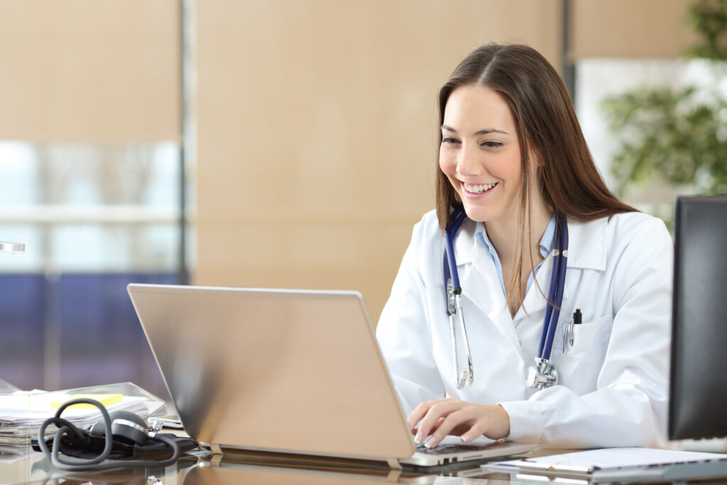 Why Your Patient Messaging Software Needs Modernization Happy doctor using a laptop writing content at consultation