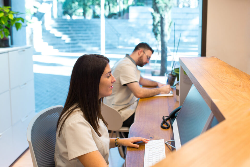 How Practices Can Improve Medical Staff Efficiency Two receptionists working at the front desk of a health center. Health care concept.