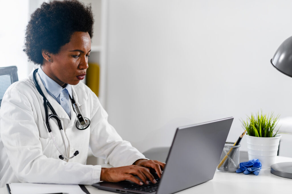 Female doctor working at her office in front of laptop computer, writing a health report