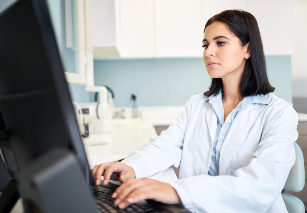 Healthcare Technology Challenges For Independent Practices One confident and focused young caucasian doctor using a computer to browse the internet in a clinic. A medical professional wearing a labcoat and updating patient reports on a desktop in her hospital.