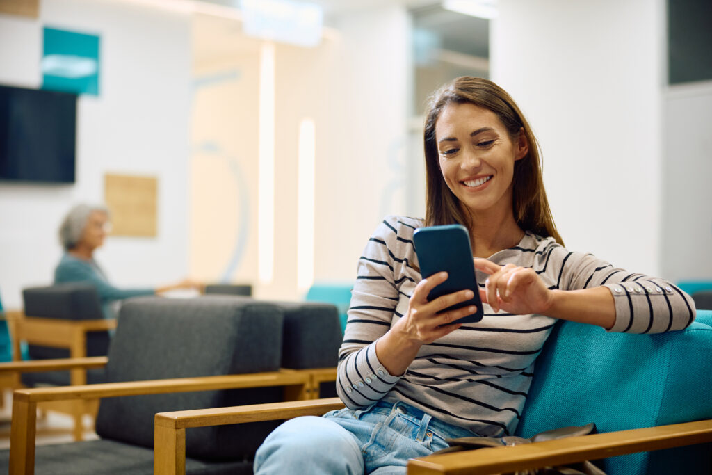 Streamlining the Transition to New Patient Portal Software Happy woman texting on mobile phone while waiting for medical appointment at clinic.