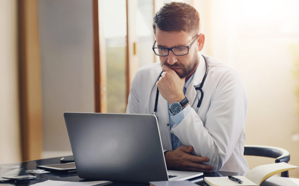 How Better Clinical Documentation Improves Billing Workflows Male person, doctor and laptop with thinking, ideas and planning in office as medical professional. Man, pediatrician and diagnosis, telehealth and technology for patient records, medicine or surgery.