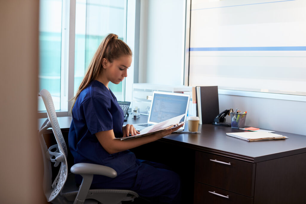 How AI Clinical Documentation Supports Financial Workflows Nurse Wearing Scrubs Working At Desk In Office
