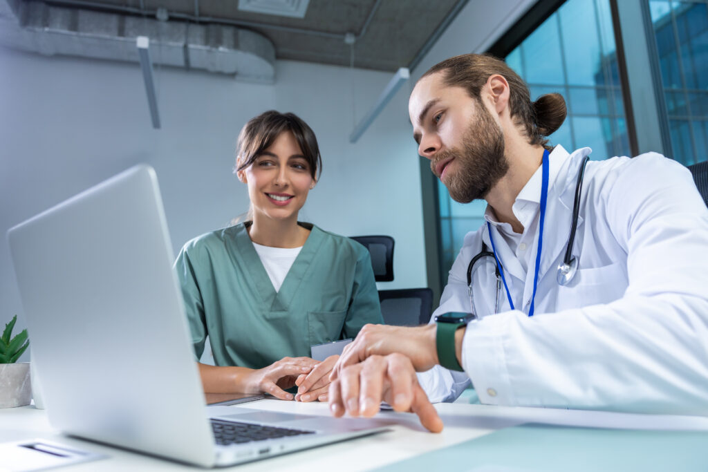 Female practitioner working with msn doctor in clinic using computer to analyze patient data and discuss medicine
