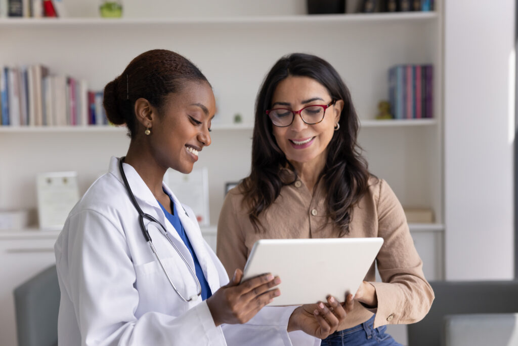 Why Front-Office Patient Communication Workflows Matter Smiling African general practitioner using tablet, showing to 60s woman patient diagnostics result, treatment plan or procedure, give recommendation, share good health news during her visit in clinic