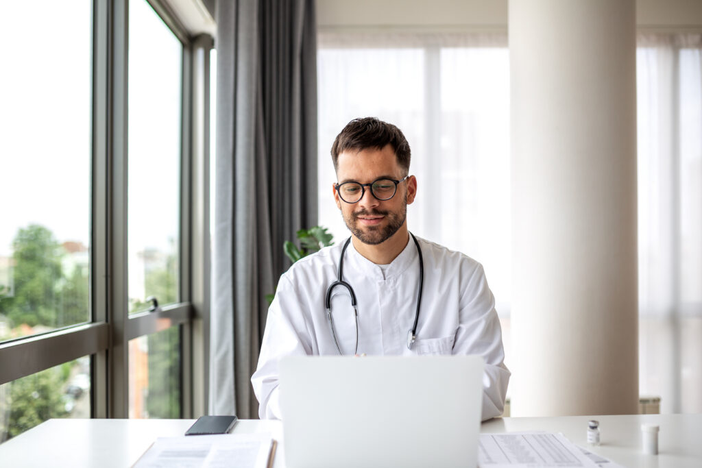 Intelligent Scheduling to Reduce No-Shows Professional Doctor Using Laptop for Telemedicine in Modern Clinic. Young Male Physician in White Coat with Stethoscope Working Online, Telehealth, Healthcare and Medical Technology Concept.