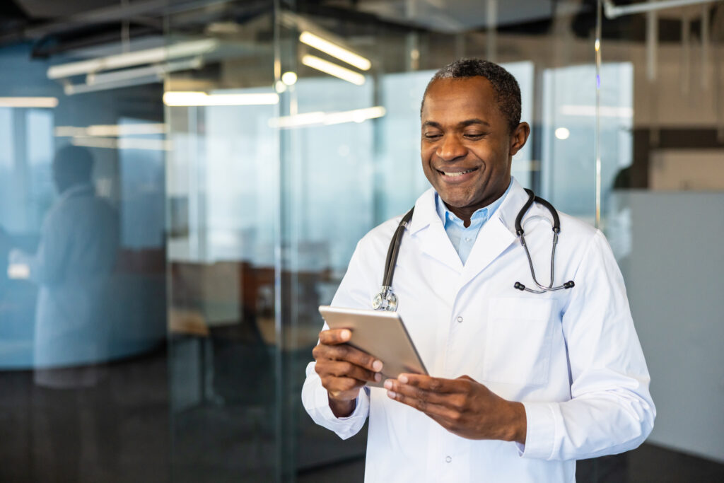 Why AI Clinical Documentation Software Is the New Standard African american male doctor in a white lab coat with stethoscope smiling while using a digital tablet modern telemedicine care, professional healthcare consultation in clinic