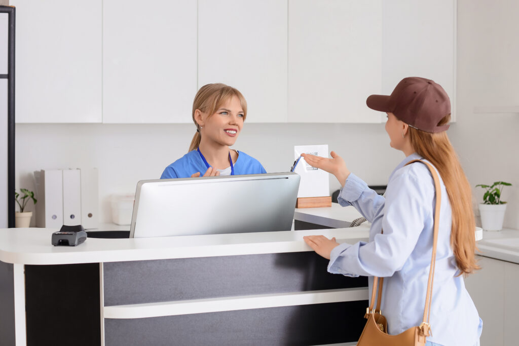 Friendly medical receptionist assisting patient at clinic front desk with digital payment option