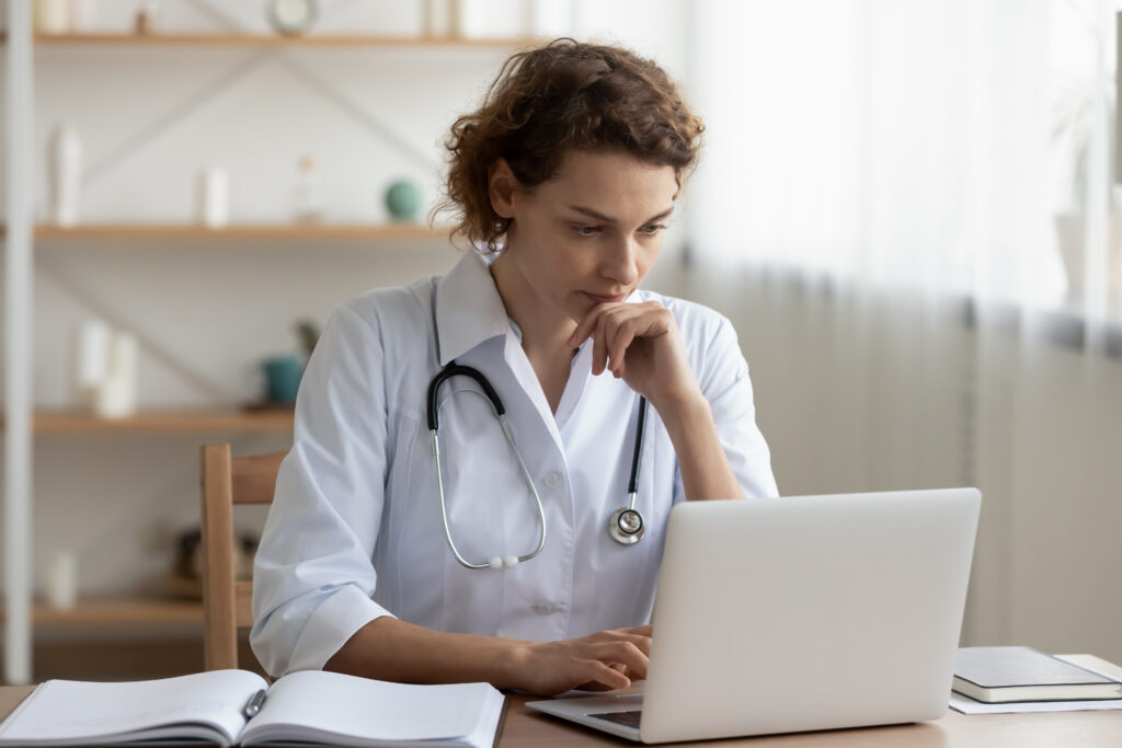 Why Workflow Simplicity Is Vital for Independent Practices Concerned young female Caucasian doctor in white medical uniform sit at desk in hospital work on laptop, focused woman nurse or GP busy fill anamnesis on computer gadget, medicine, technology concept