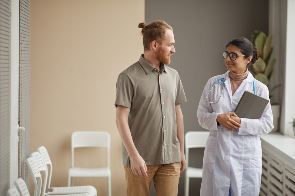 How AI Patient Summaries Improve Clinical Documentation Young female doctor in white coat talking to male patient while they walking along the corridor at hospital