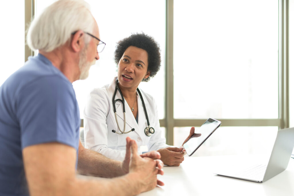 Why AI Clinical Documentation Software Is the New Standard Serious retired man consulting with younger female doctor at the checkup meeting in the hospital. Experienced general practitioner giving healthcare medical advices to mature patient