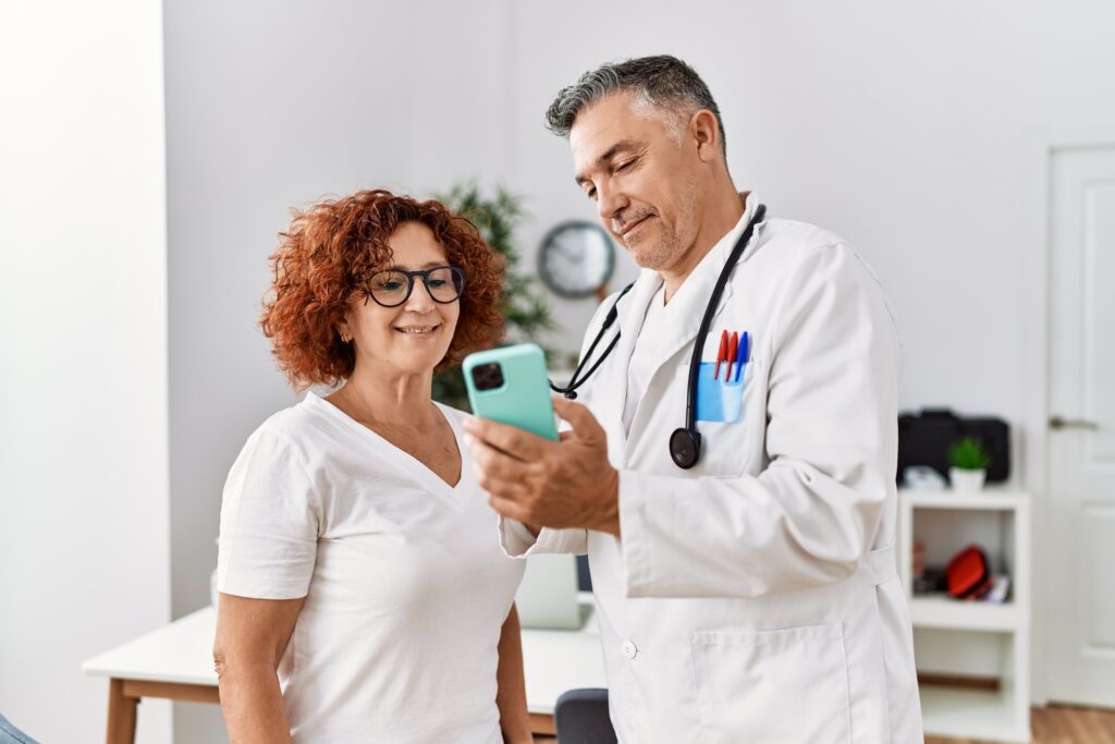 How AI Patient Summaries Improve Clinical Documentation Middle age man and woman wearing doctor uniform using smartphone having medical consultation at clinic