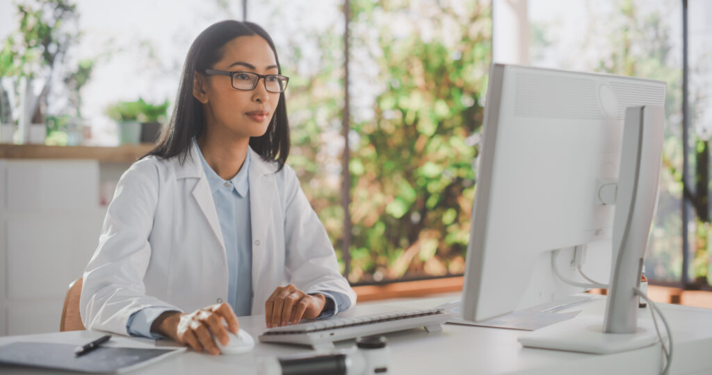 Intelligent Scheduling to Reduce No-Shows Portrait of an Asian Medical Health Care Professional Working on Desktop Computer in Hospital Office. Female Clinic Physician Appointing Prescriptions Online, Updating Electronic Health Records