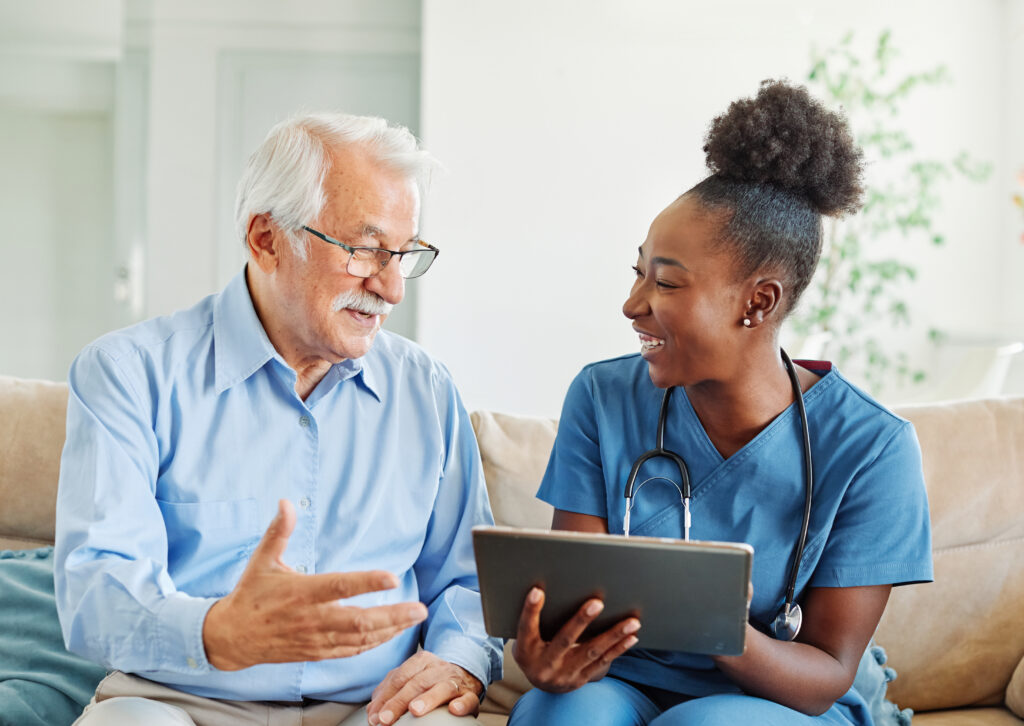 Doctor or nurse caregiver showing a tablet screen to senior man and laughing at home or nursing home